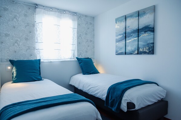 A bedroom with two beds, a window with sheer curtains, and a wall-mounted abstract painting. - Les Sycomores: a spacious 8-person vacation home with a spa, a 5-minute walk from the ocean (Ver-sur-Mer)