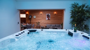 A hot tub with water jets, a wooden wall with a clock, a sofa, and a potted plant. - Les Sycomores large 8-person gîte with spa, 5-minute walk from the sea (Ver-sur-Mer)