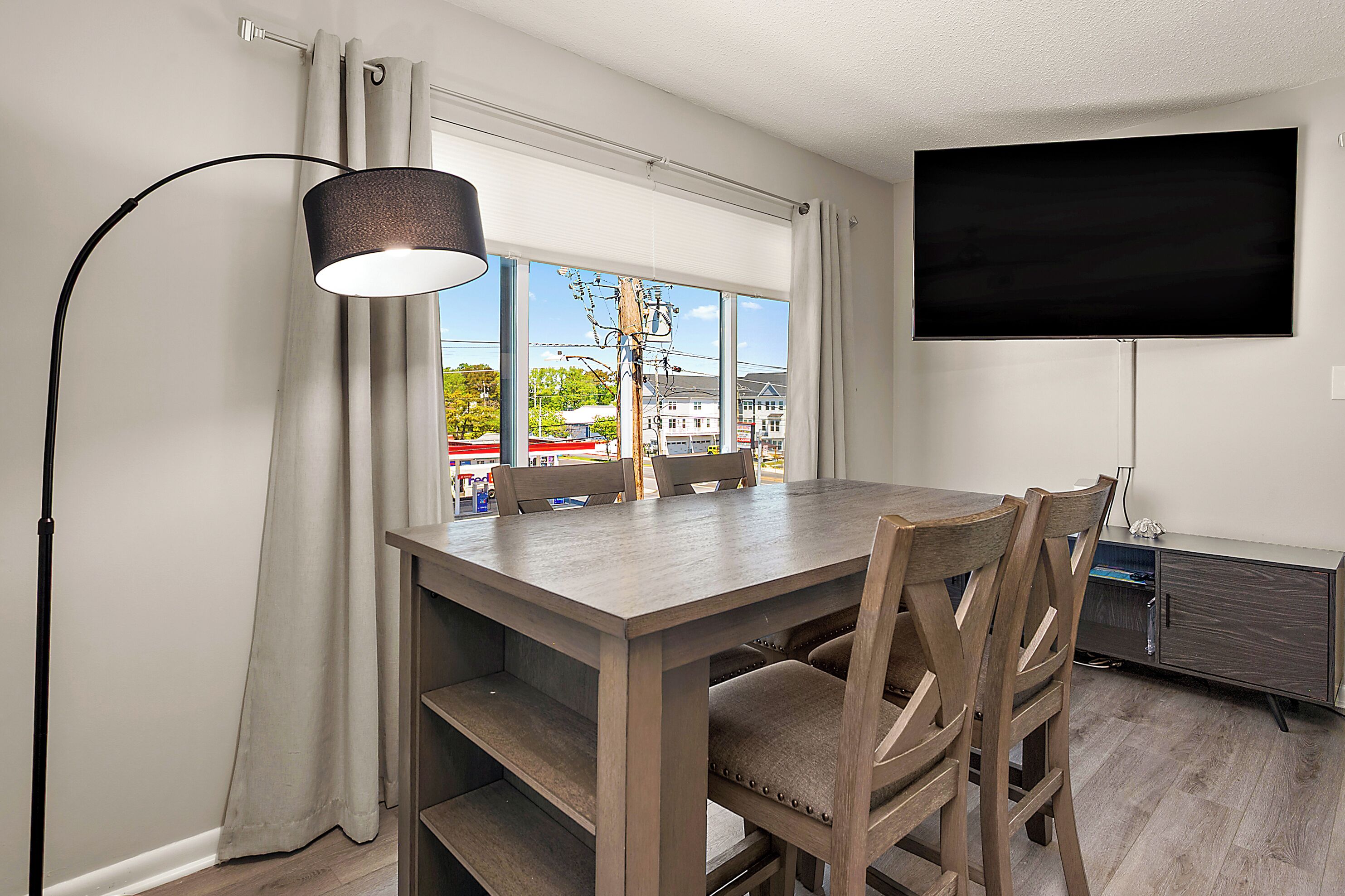 A dining area with a table, chairs, a lamp, a TV, and a window with curtains.