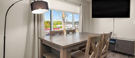 Ein Essbereich mit Tisch, Stühlen, einer Lampe, einem Fernseher und einem Fenster mit Vorhängen.