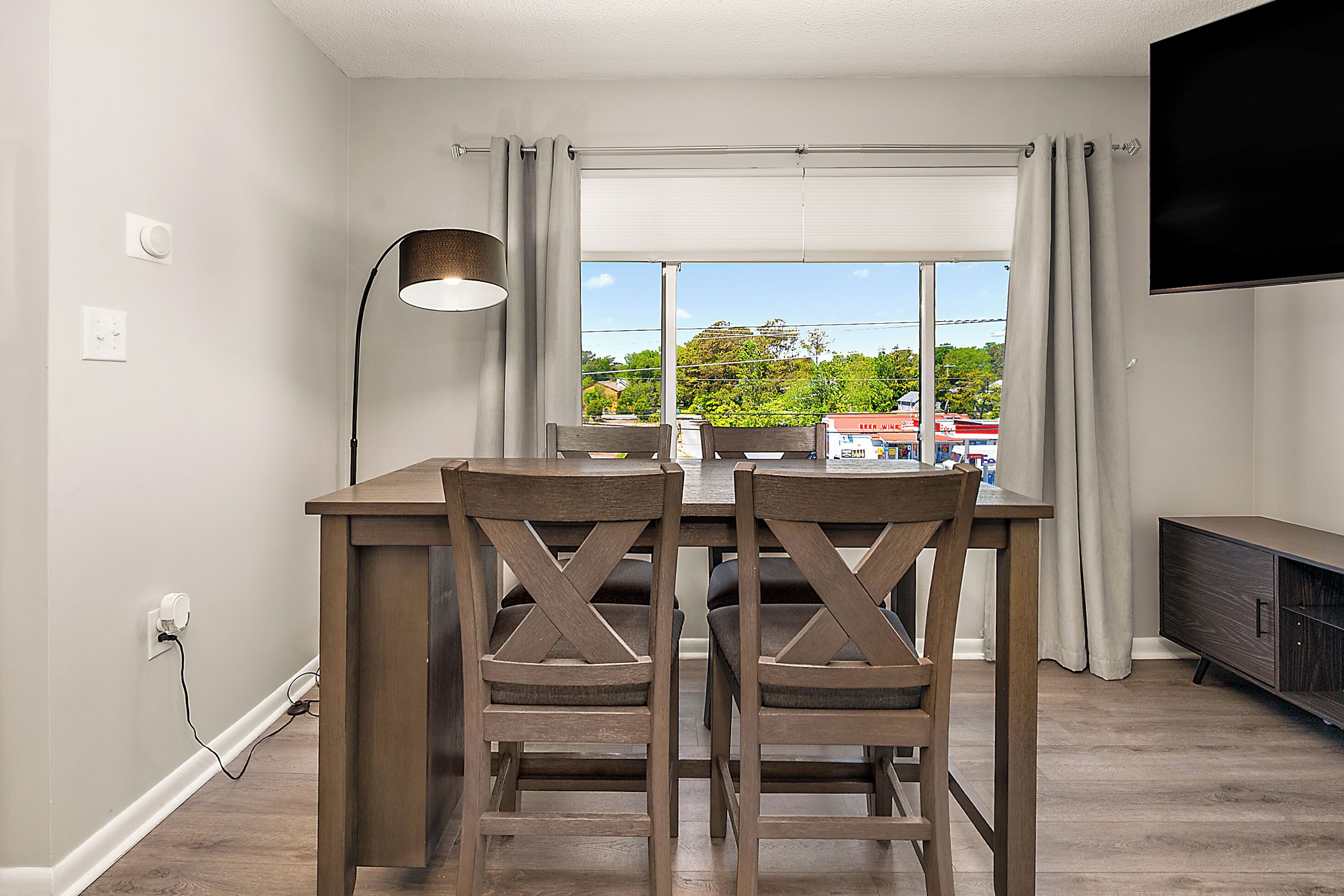 A dining area with a table and chairs, a lamp, a TV, and a window with curtains.
