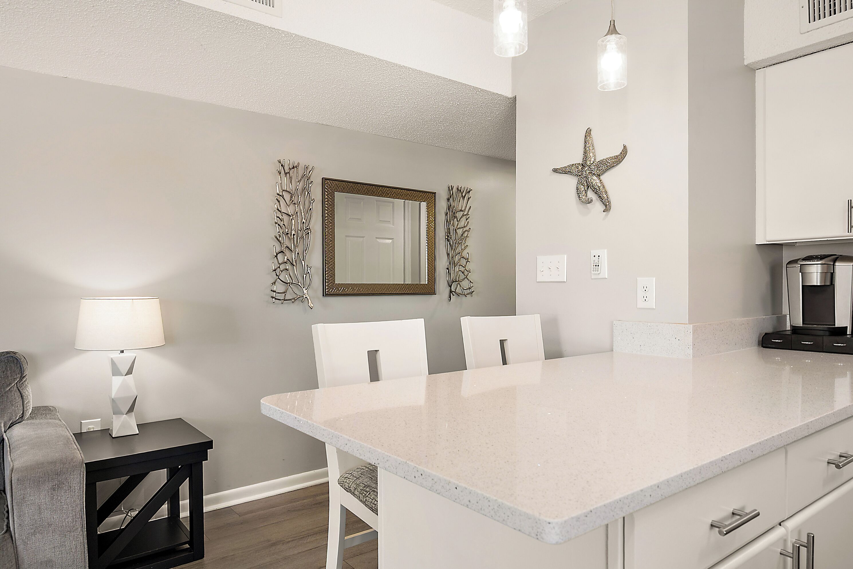 A kitchen with a large island, white chairs, a coffee maker, and a starfish decoration on the wall.