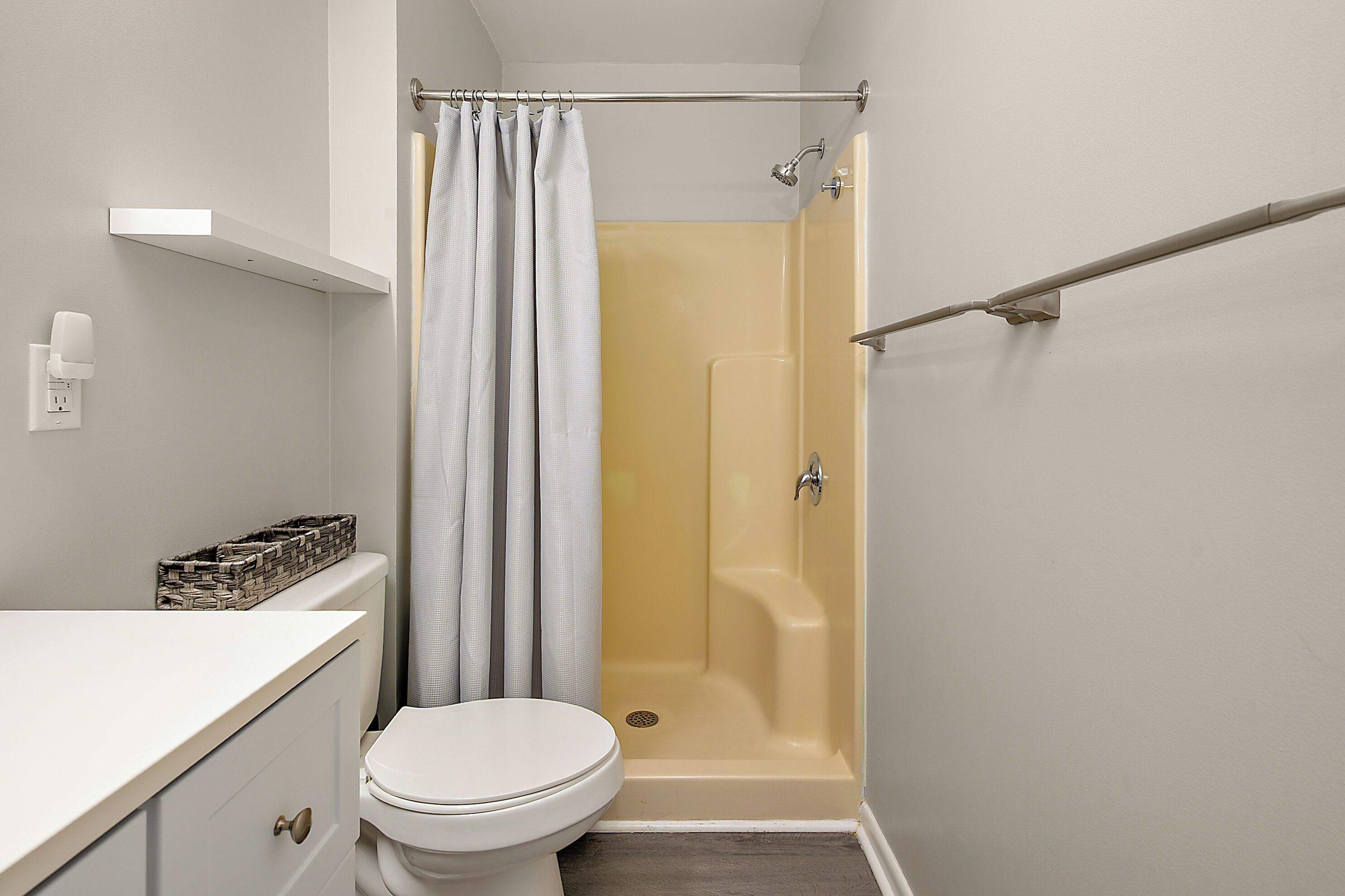 A bathroom with a toilet, a shower, a towel rack, and a soap dispenser.