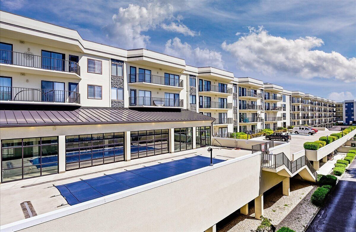 A modern multi-story residential building with balconies, large windows, and a rooftop pool area.