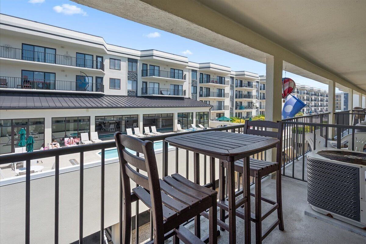 A balcony with a table and chairs, overlooking a pool and adjacent buildings.