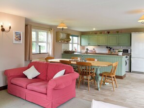A cozy living room with a red sofa, a dining table with chairs, and a kitchen area with green cabinets and a white refrigerator.