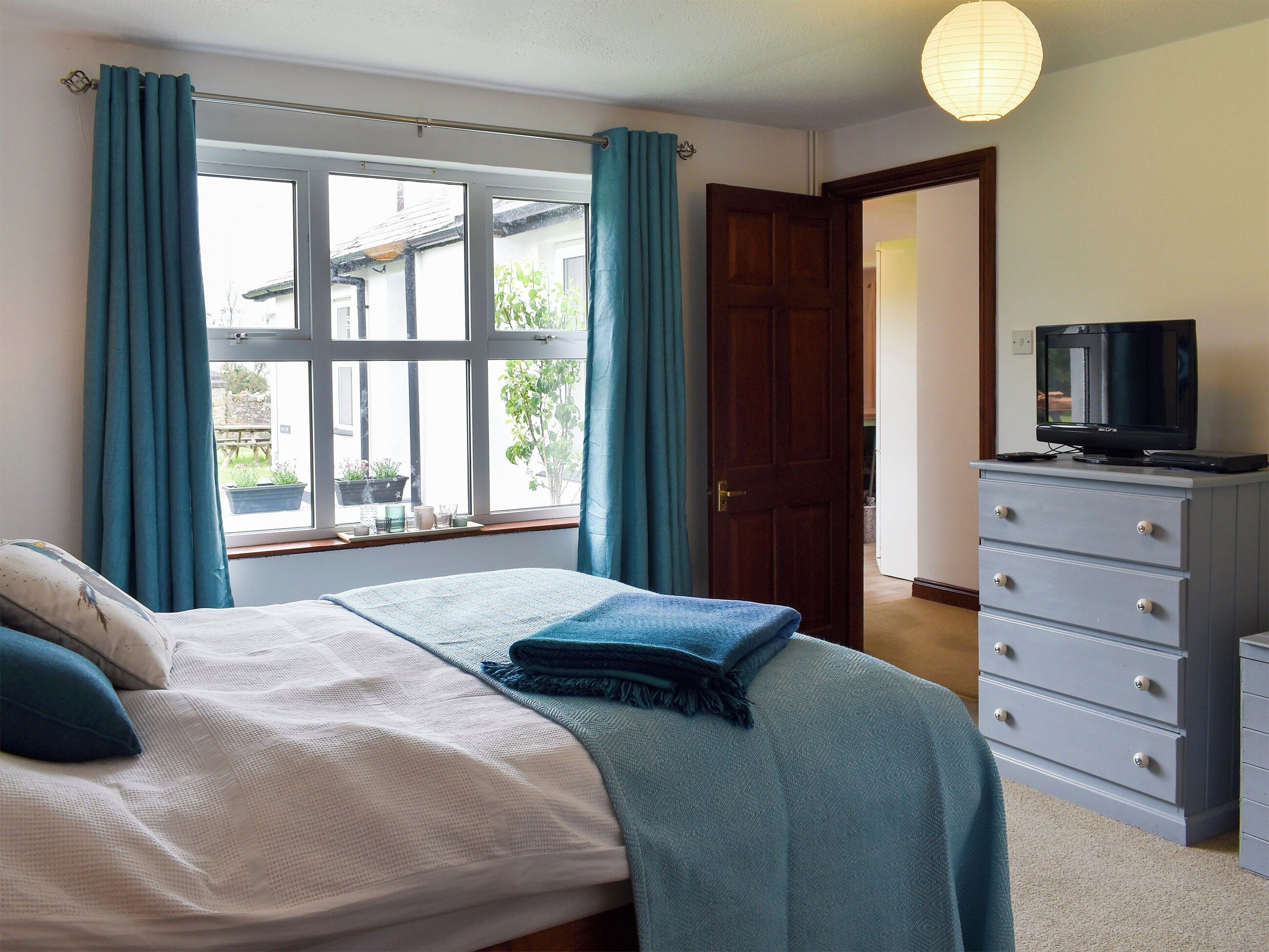 A bedroom with a bed, a dresser, a television, and a window with curtains.