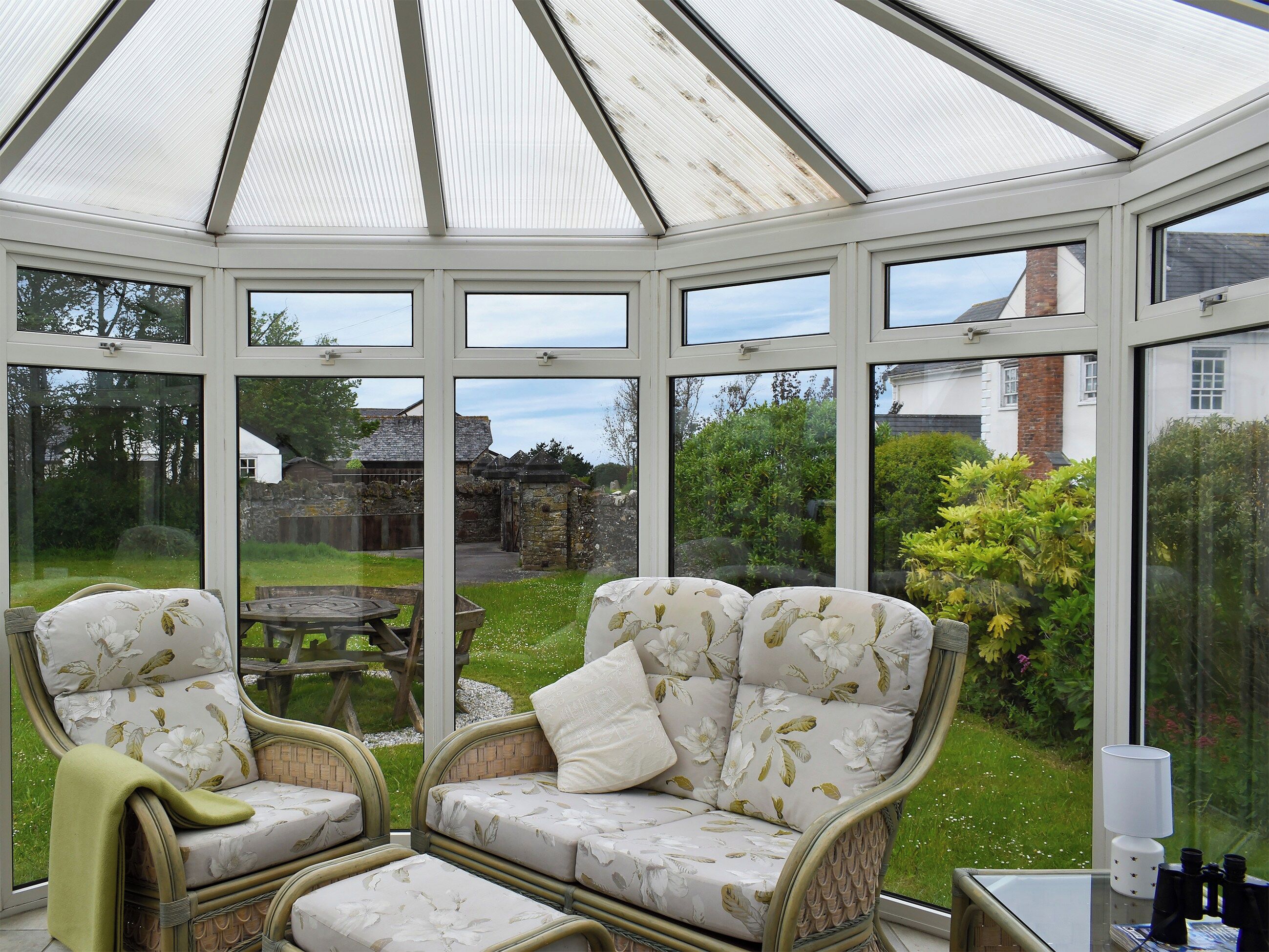 A conservatory with wicker furniture and a view of the garden.