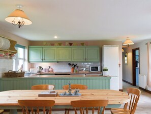A kitchen with green cabinets, a wooden dining table, and a white refrigerator.