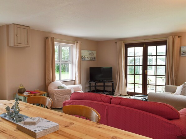 A living room with a sofa, a television, a dining table with chairs, and a window with curtains.