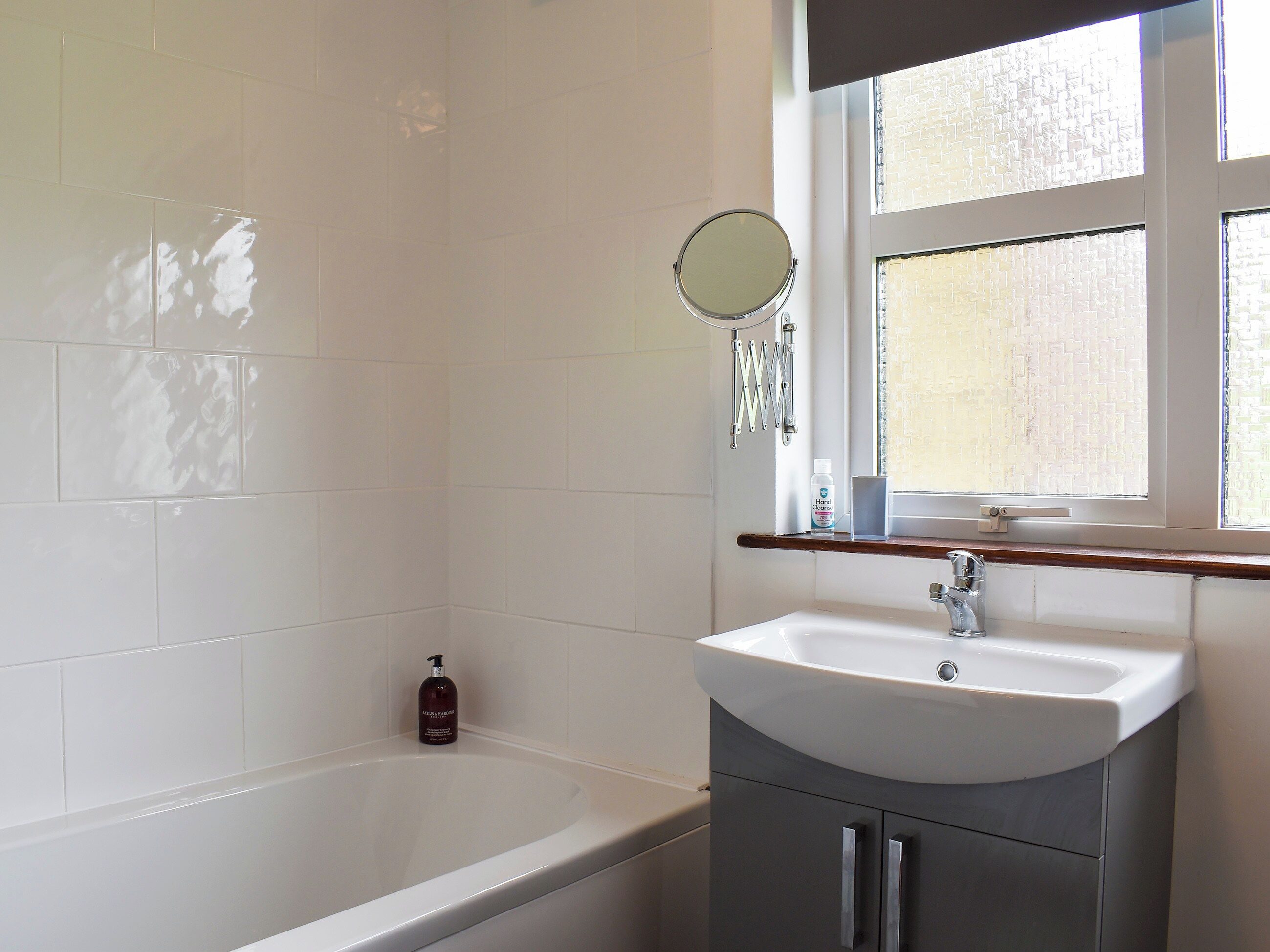 A bathroom with a bathtub, a sink, a mirror, and a window.