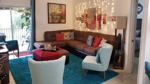 Ein Wohnzimmer mit Ecksofa, blauem Teppich, Deckenventilator und Wandleuchte.