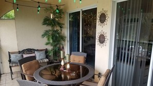 Ein überdachter Patio-Bereich mit Korbmöbeln, einem Glastisch und dekorativer Beleuchtung.