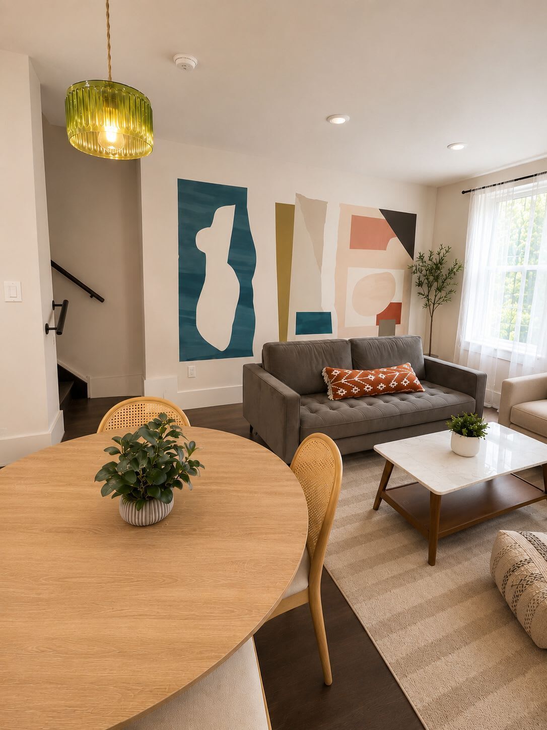 A modern living room with a round dining table, a grey sofa, a coffee table, and abstract wall art.