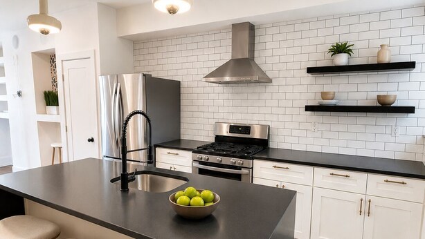 Una cocina moderna con una isla central, electrodomésticos de acero inoxidable e iluminación colgante.