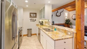 A modern kitchen with a stainless steel refrigerator, granite countertops, and a wooden accent wall. - New Listing! Three Bedroom Apartment, Sleeps 6, Steps to Ski Access (Whitefish)
