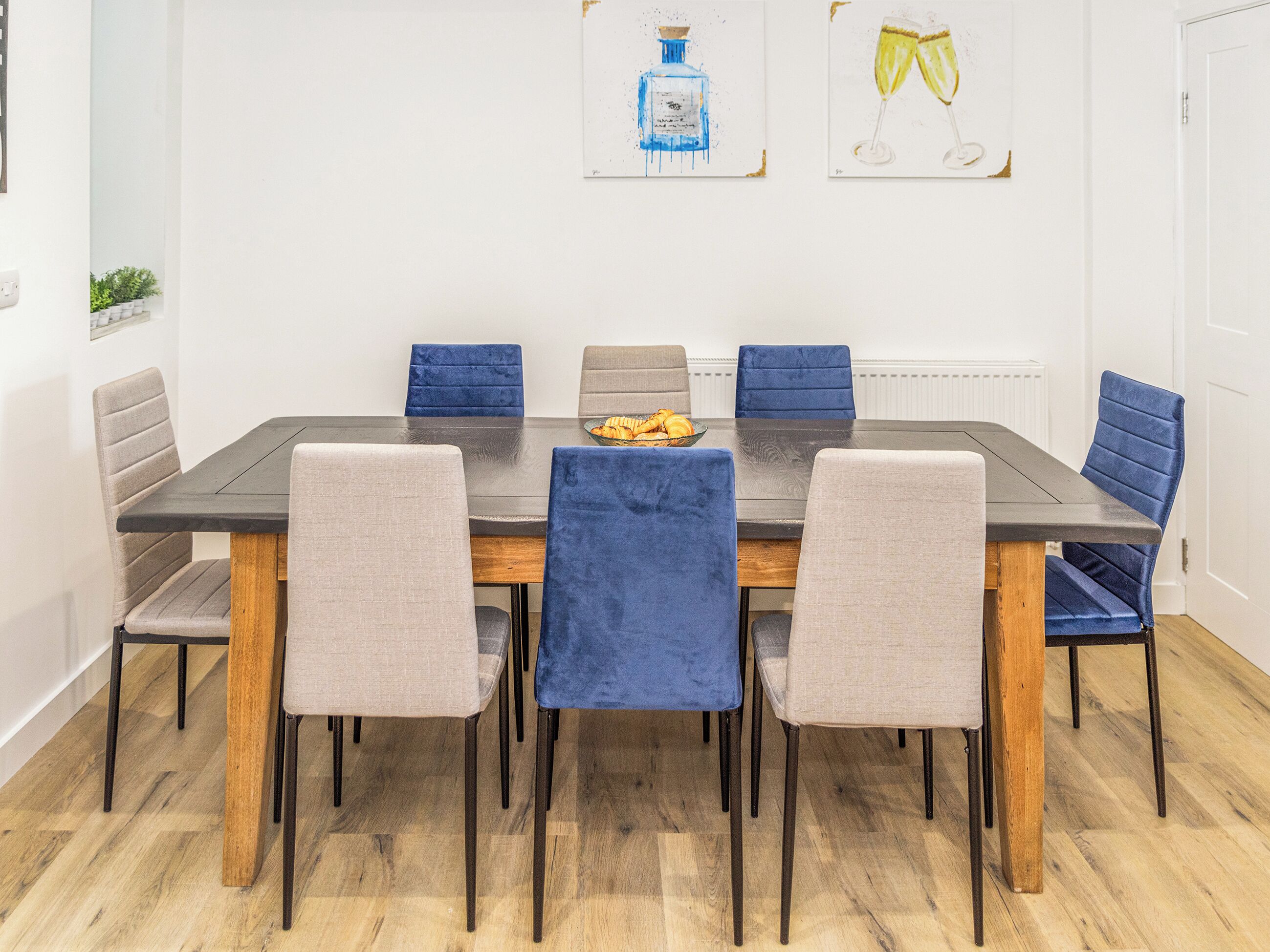 A dining area with a rectangular table, six chairs, and two wall-mounted artworks.