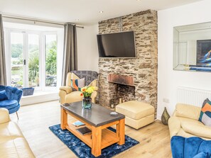 A living room with a stone wall, a flat-screen TV, a sofa, a coffee table, and a view through a large window.