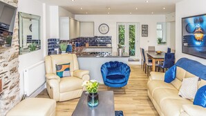 Ein modernes Wohnzimmer mit Sofa, Sessel, Couchtisch und einem Essbereich mit Stühlen und Tisch.