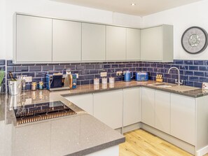 A modern kitchen with white cabinets, a blue tiled backsplash, a built-in microwave, a toaster, and a sink.