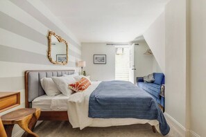 A bedroom with a bed, bedside table, lamp, and a mirror.