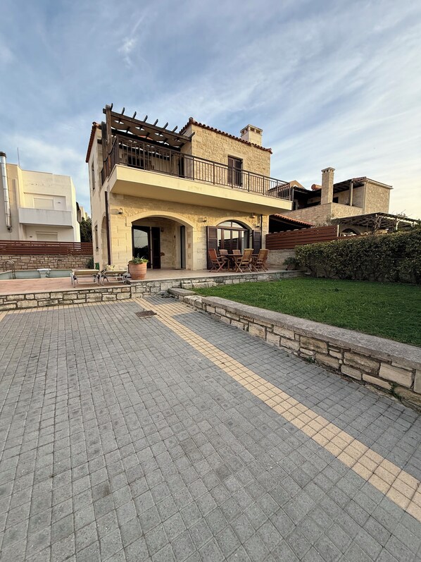 A two-story house with a balcony, a paved courtyard, and a grassy area. - Villa with Ocean View and Private Pool (Sfakaki)