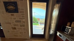 Una cocina con refrigerador, microondas y cafetera. Hay una puerta que da a un balcón con vistas al cielo y al follaje.