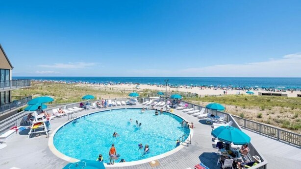 Un espace piscine avec vue sur la plage, agrémenté de chaises longues et de parasols.