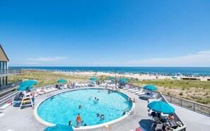 A pool area with a view of the beach, surrounded by lounge chairs and umbrellas.