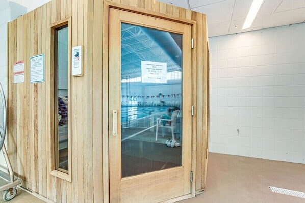 A wooden sauna room with a glass door, a towel rack, and a sign indicating sauna use.