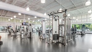 Une salle de sport spacieuse, dotée de divers appareils d’exercice et d’un plafond haut éclairé par des luminaires industriels.