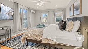 Een slaapkamer met een bed, een bureau, een televisie en een plafondventilator.