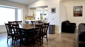 A modern kitchen with white cabinets, a dining area with a wooden table and chairs, and a black trash can. - Welcome to Oasis On The Links! (Paso Robles)
