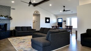 A spacious living room with a fireplace, dark sofas, a patterned rug, and ceiling fans. - Welcome to Oasis On The Links! (Paso Robles)