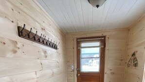 A hallway with wooden walls, a black mat at the entrance, a ceiling light, and a door with a window. - The Guides House • Cozy Main St Stay with Porch Views (Old Forge)