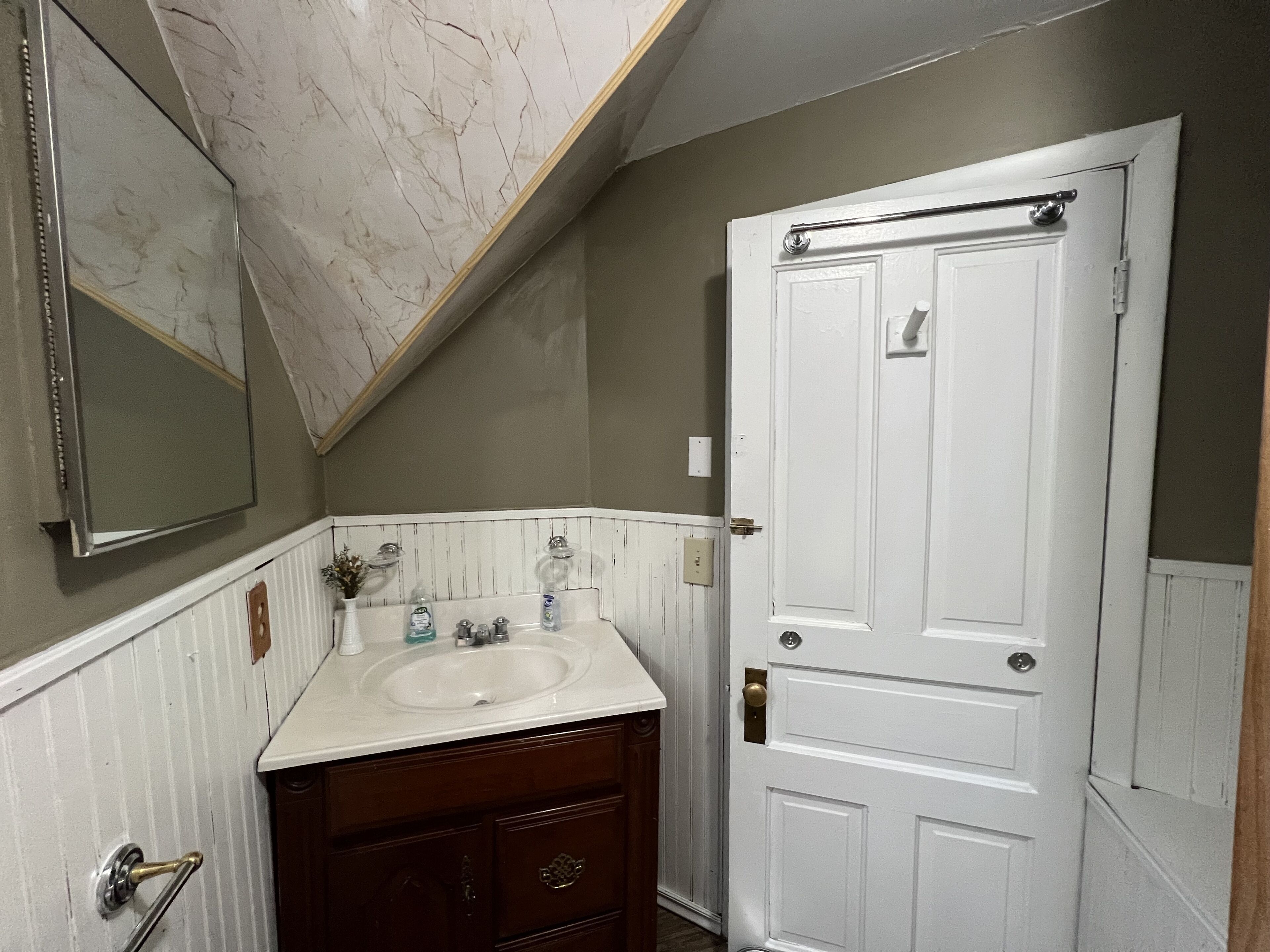 A bathroom with a white sink, wooden vanity, and a white door.