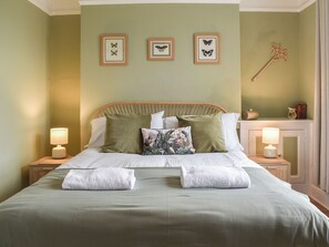 Una cama bien tendida con almohadas, una lámpara de noche y una pared decorada con ilustraciones de mariposas.