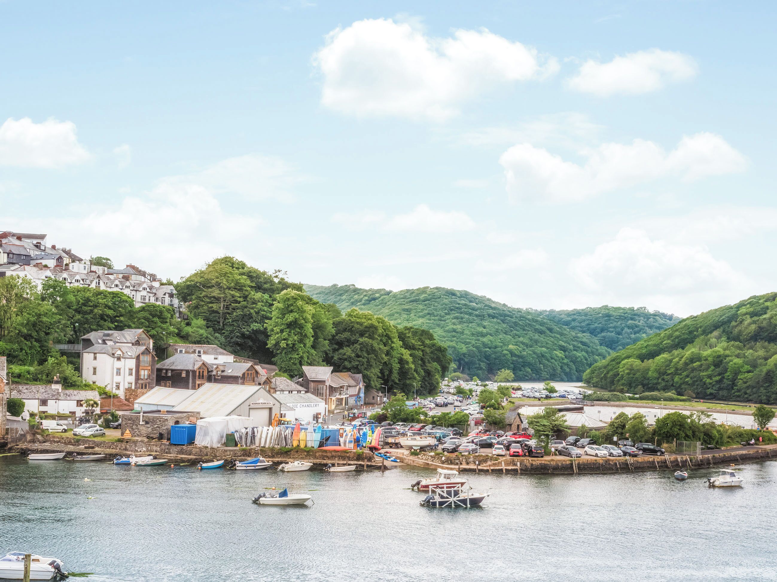 A coastal town with boats docked along the waterfront, buildings with visible signage, and a hilly backdrop.