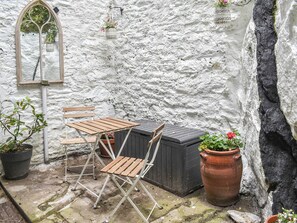 Un espacio al aire libre rústico con una mesa y sillas de madera, plantas en macetas y un muro de piedra.