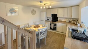 Une cuisine moderne avec des meubles blancs, une table à manger avec des chaises, une horloge et un escalier.