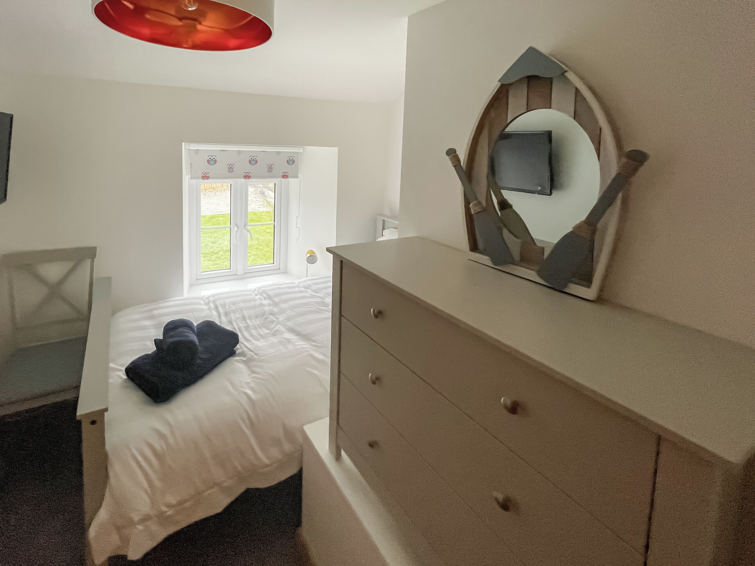 Ein Schlafzimmer mit Bett, Kommode, Spiegel, Fenster und Stuhl.