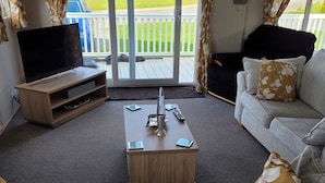 A living room with a TV, a coffee table, and a sofa. There is a sliding glass door leading to a balcony. - Remarkable 3-bed House in Hull (Hull)