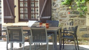 Un espacio para comer al aire libre con un muro de piedra, una mesa de madera y sillas de metal.