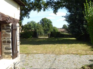 Un bâtiment en pierre avec une allée de gravier menant à une zone herbeuse agrémentée d’arbres et d’une clôture.