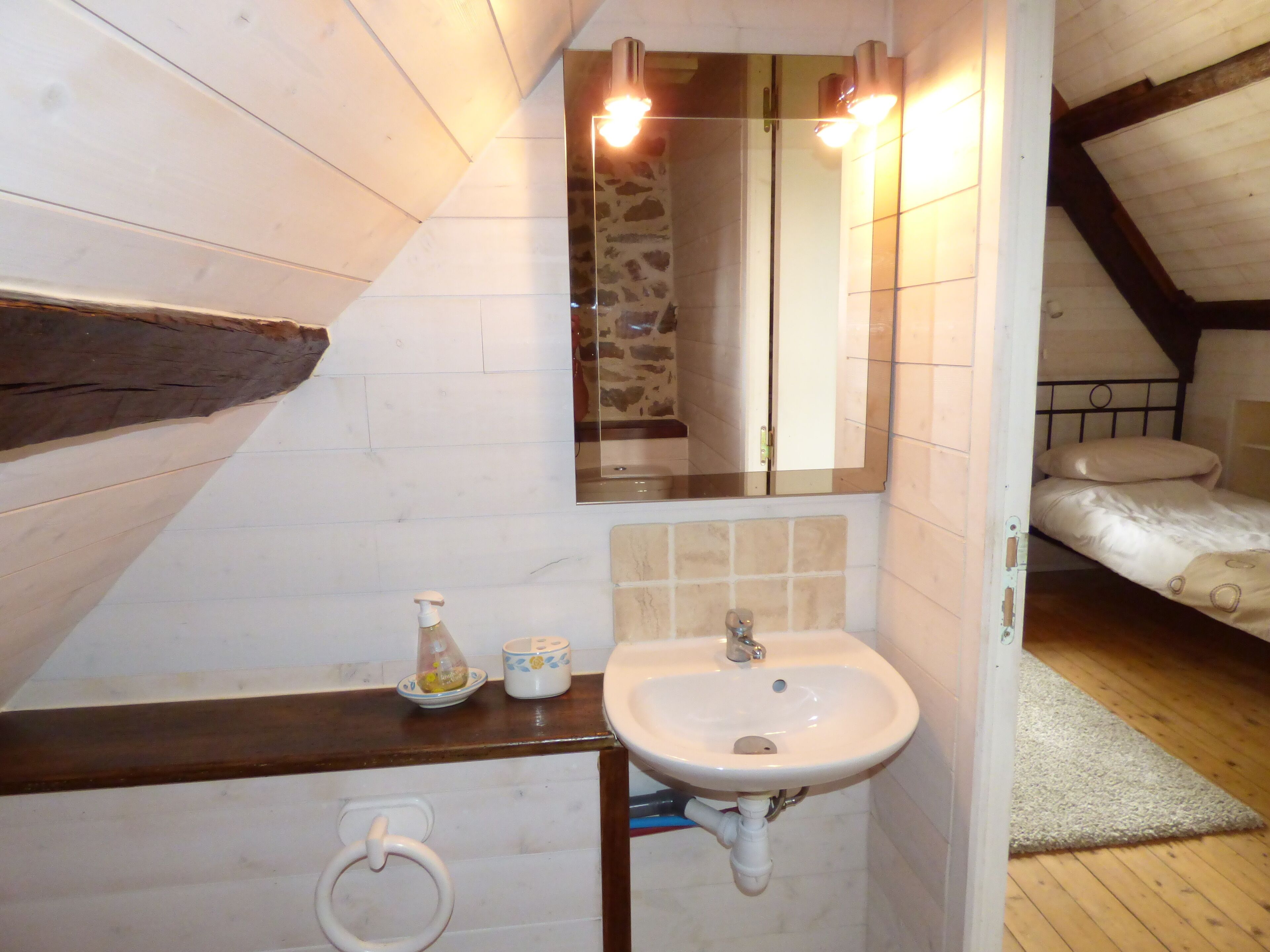 A small, cozy bathroom with a wooden ceiling, a white sink, and a mirror above it.