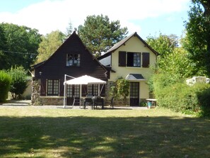 Een huis met twee verdiepingen, een stenen fundering en een houten gevel. Er is een terras met buitenmeubilair en een witte parasol.