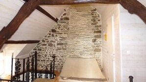 Un espacio bajo de áticos estrecho con pared de piedra, vigas de madera y piso de madera.
