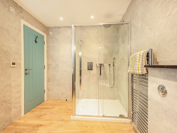 Une salle de bain moderne avec une douche à parois de verre, un plancher en bois et une porte de couleur turquoise.