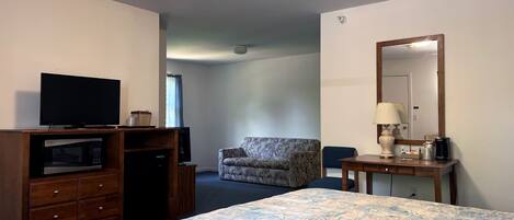 Ett hotellrum med en säng, en tv, ett skrivbord med en lampa, en stol och en mikrovågsugn.