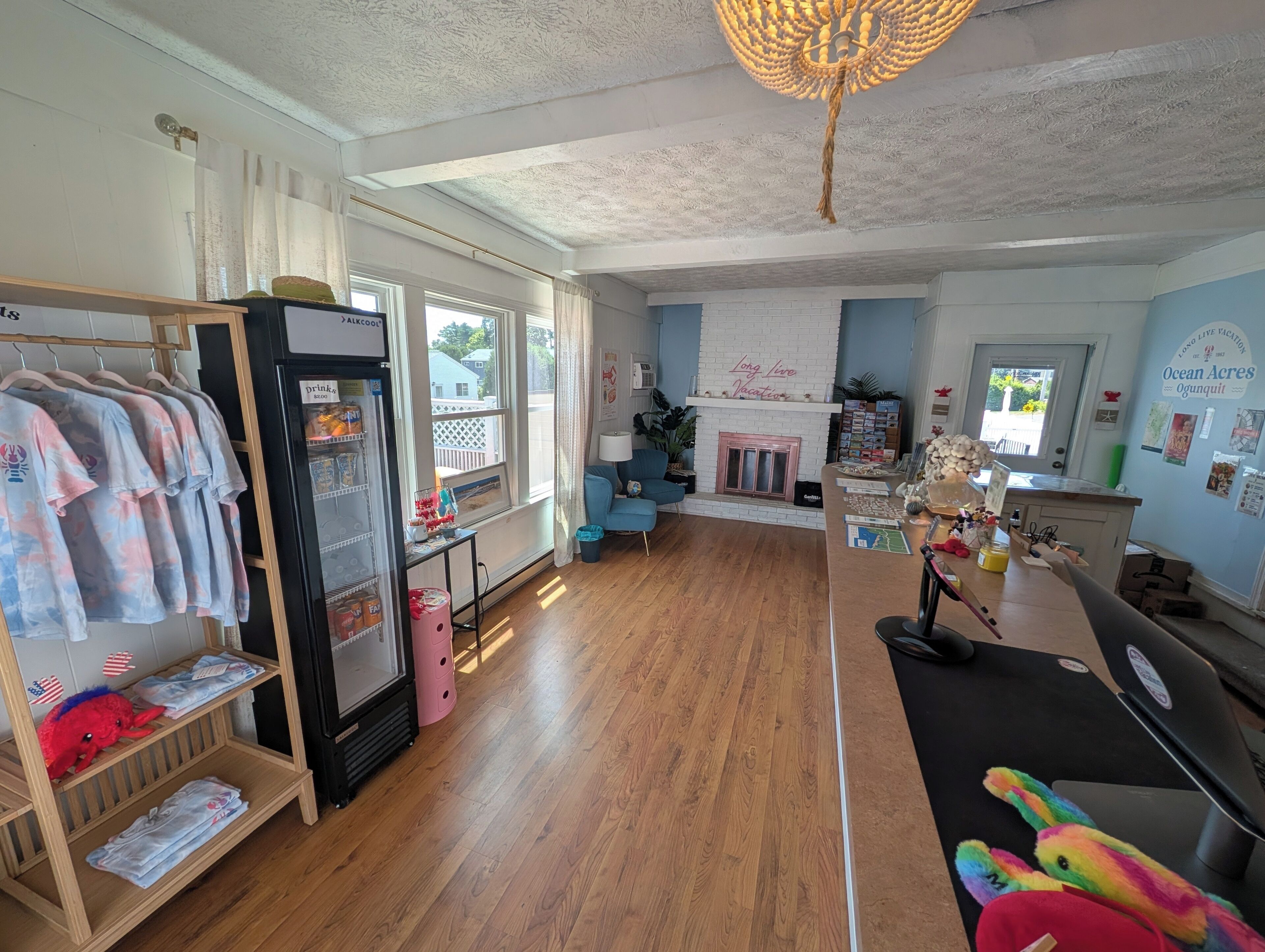 A room with a wooden floor, a white brick fireplace, a blue sofa, a refrigerator, and a shelf with children's items.